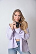 Charming young woman with blonde hairs and blue eyes. Female model wearing purple top and blue jeans. Woman holding vintage camera.