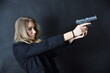 Charming young woman with blonde hairs and blue eyes, black background. Female model with gun in her hands.