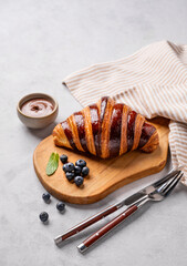 Wall Mural - Fresh croissant with chocolate on a cutting board on a light background with a blueberries. Delicious homemade breakfast concept.