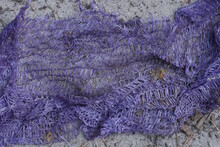 A Piece Of Old Crumpled Purple Plastic Mesh Lies On The Gray Sand On The Street