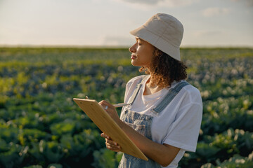 Wall Mural - Female agronomist making notes in clipboard on cabbage field during harvesting. Agricultural concept