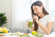 © KMPZZZ - Green detox juice concept, Beautiful asian young woman holding vegetable smoothie glass with straw for diet at home. Happy girl drinking healthy meal food for weight loss. Lifestyle, vegan nutrition.