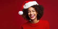 Happy Smiling Young African American Woman In Santa Hat Over Red Background. She Is Laughing And Looking At Camera.