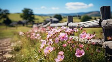 A Charming Country Path Edged With Pink Blossoms, With A Wooden Fence Leading Towards Rustic Farmhouses Amidst A Serene Pastoral Landscape Under A Bright Blue Sky.