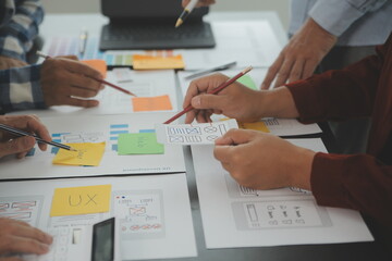 Close up ux developer and ui designer brainstorming about mobile app interface wireframe design on table with customer breif and color code at modern office.Creative digital development agency