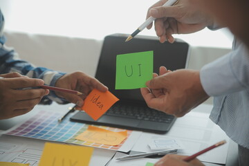Close up ux developer and ui designer brainstorming about mobile app interface wireframe design on table with customer breif and color code at modern office.Creative digital development agency