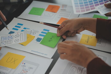 Close up ux developer and ui designer brainstorming about mobile app interface wireframe design on table with customer breif and color code at modern office.Creative digital development agency