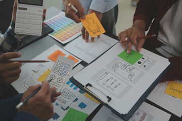 Close up ux developer and ui designer brainstorming about mobile app interface wireframe design on table with customer breif and color code at modern office.Creative digital development agency