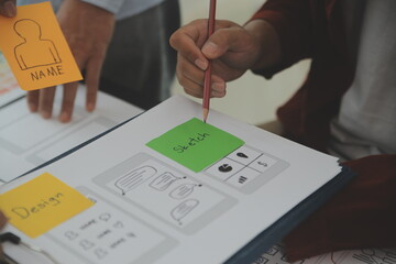 Close up ux developer and ui designer brainstorming about mobile app interface wireframe design on table with customer breif and color code at modern office.Creative digital development agency