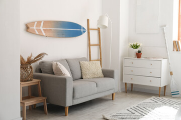 Interior of light room with surfboard, sofa and drawers