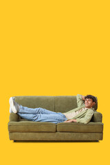 Poster - Young man resting on sofa against yellow background