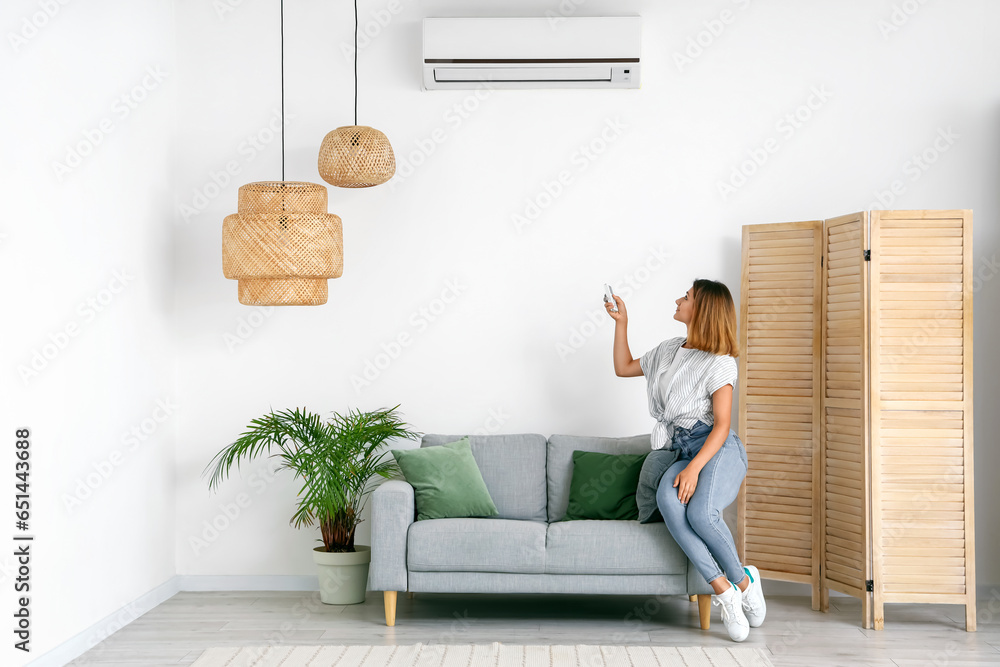 Young woman switching on air conditioner at home