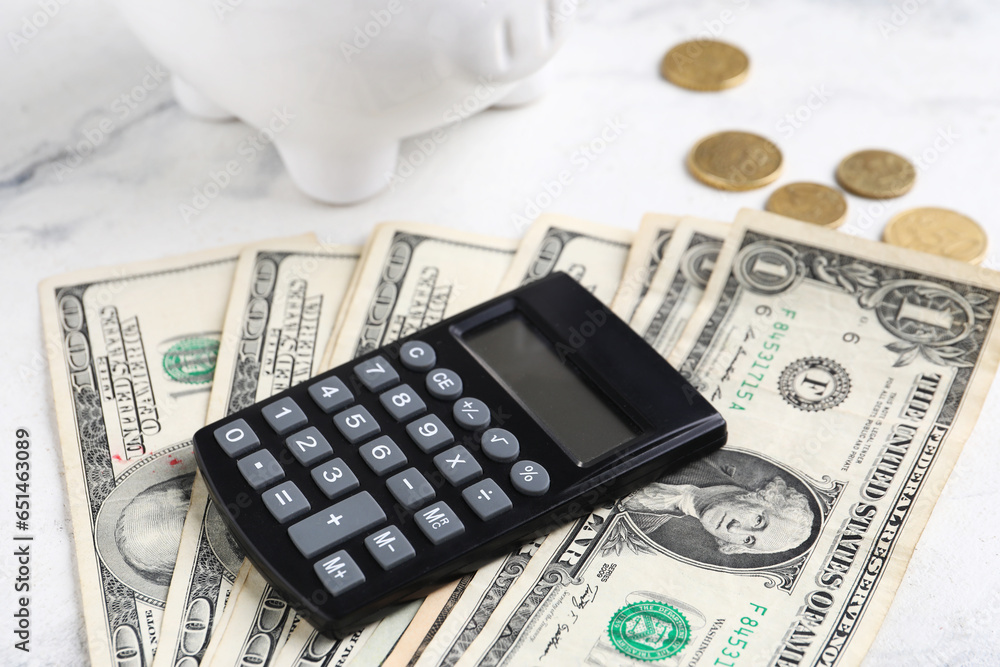 Calculator, dollar banknotes and coins on white marble background