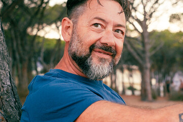 Wall Mural - Side closeup portrait of adult man with beard smiling and enjoying relax time at the park. Happy and serene people with cheerful expression. Good day. Handsome male 50 years old outside. Nature place