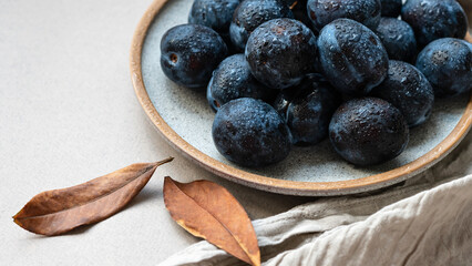 Wall Mural - Fresh plums with water drops on plate, closeup, brown fall leaves on neutral beige table background