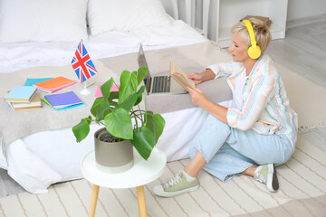 Canvas Print - Mature woman with headphones learning English language online in bedroom