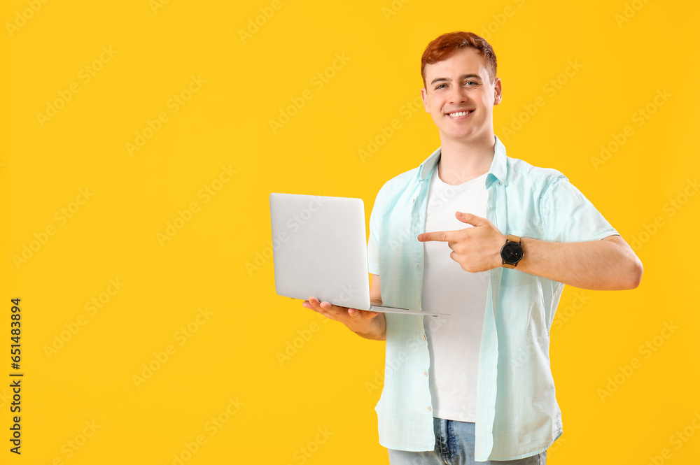 Happy young redhead man pointing at laptop on yellow background. Black Friday sale