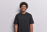 Fototapeta  - People positive emotions concept. Studio waist up of young happy smiling broadly Hindu man standing in centre isolated on white background wearing black casual t shirt looking straight at camera