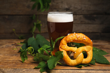 Soft pretzel, hop leaves and glass of beer on wooden background