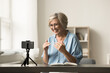 canvas print picture - Cheerful senior elder influencer woman working on shooting for blog, recording selfie video at home, speaking at cellphone camera fixed on tripod, smiling, broadcasting online