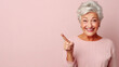 Senior beautiful woman pointing aside and smiling with pink background and copy space