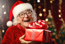 Happy Old Woman In Santa Claus Hat Receiving Christmas Present At Home. Christmas Concept
