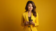 © amila - Young elegant business woman using her phone in yellow background