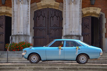 An Antique Blue Car Standing In Front Of The Church, Decorated With Flowers - A Wedding Car
