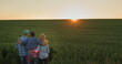 Happy family of farmers admiring the sunset over a field of wheat