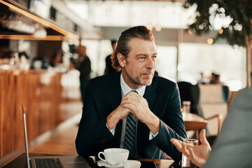 Wall Mural - Middle aged Caucasian businessman enjoying a cup of coffee while on a meeting with a coworker in a café decorated for Christmas and the new year holidays