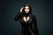 Sexy chubby plus size fashion model with large breasts in black tight dress, fat curvy woman on gray background