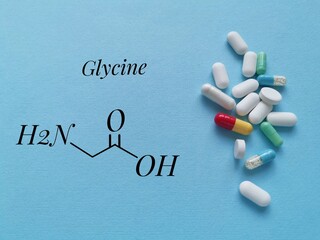Structural chemical formula of glycine with pills on blue background. Glycine is an amino acid, a building block for protein. It can also be found as a dietary supplement in capsule or tablet form.