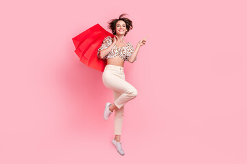 Poster - Full length photo of attractive woman wear top pants jumping hold shopping bags indicating empty space isolated on pink color background