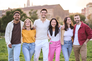 Wall Mural - Happy young beautiful people enjoying summer sunny day spending time outdoors and having fun together. Joyful and smiling multiracial friends hugging standing in city park. Diverse group portrait.