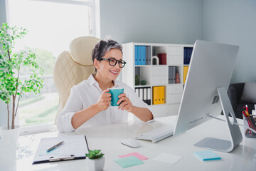 Photo of using creative director company producer mature woman white formal shirt drinking morning tea check stats isolated in office