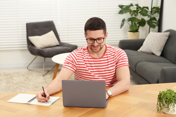 Canvas Print - Man working with laptop at wooden table in room