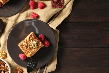 Piece of delicious layered honey cake with raspberries served on wooden table, flat lay. Space for text