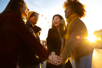 Wall Mural - Multiracial young people stack hands in a circle as symbol of community and friendship outdoors on a winter day.