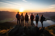 Company Of People With Backpack Standing On Top Of A Cliff In The Summer Mountains At Sunset And Enjoying The Nature View