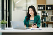 © Nuttapong punna - Beautiful Asian woman using laptop and tablet while sitting at her working place. Concentrated at work. in office..