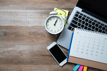 close up of calendar, alarm clock, computer laptop on the wooden table background, planning for business meeting or travel planning concept