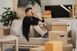 © NINENII - Exhausted Male sit rest on sofa in living room near heap of cardboard boxes feel unmotivated to unpack their belongings. Financial problem, debt and eviction, house debt bankrupt stress concept.