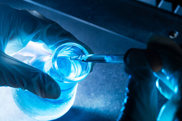 Wall Mural - blue science experiment bottle,bottle of water in the hand of a scientist by dropping liquid into a 