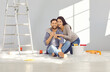 © Studio Romantic - Happy family decorating their house. Cheerful young married couple doing renovations at home. Joyful man and woman sitting on floor with paint bucket, hugging, smiling, and looking at camera