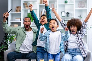 Excited family football fans watching sport tv game celebrating goal together, happy parents mom dad and little kids children supporting favorite soccer team victory at home sit on sofa