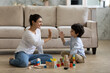 © fizkes - Happy Indian mother and 5s son giving high five, sitting on warm floor at home, smiling young mom with boy child having fun, playing with colorful wooden construction toys, spending leisure time
