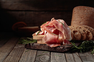 Poster - Prosciutto with bread and rosemary on an old wooden table.