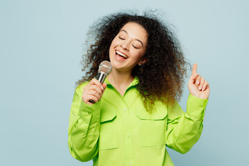 Wall Mural - Young fun happy singer latin woman she wear green shirt casual clothes sing song in microphone at karaoke club isolated on plain pastel light blue cyan background studio portrait. Lifestyle concept.