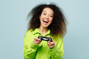 Wall Mural - Young excited latin woman she wears green shirt casual clothes hold in hand play pc game with joystick console isolated on plain pastel light blue cyan background studio portrait. Lifestyle concept.