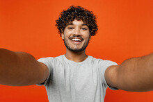 Close Up Young Smiling Satisfied Happy Indian Man He Wears T-shirt Casual Clothes Doing Selfie Shot Pov On Mobile Cell Phone Isolated On Orange Red Color Background Studio Portrait. Lifestyle Concept.